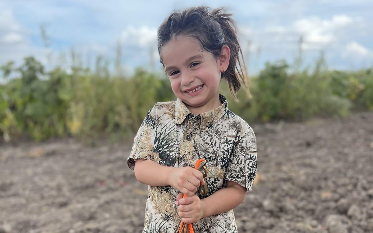 A young first-time hunter holding a strap of dove on a Valley field
